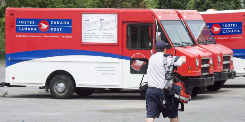 A canada post worker walks towards a fleet of company vehicles.