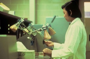 A worker in an overcoat analyzes beakers. They appear to contain samples of sand.