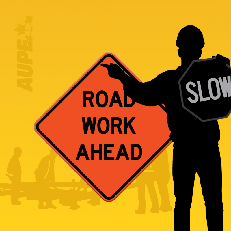 A road worker carries two signs which read &quot;Slow&quot; and &quot;Road work ahead&quot;