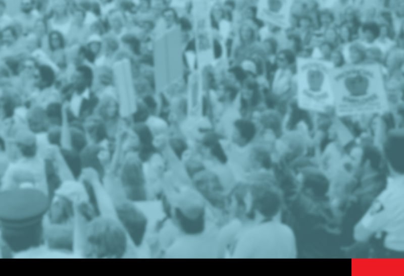 Blurred blue-scale image showing a crowd of people, some with raised fists, some holding signs